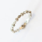 A white gold eternity wedding band featuring leaf patterns alternating with tiny bezel set diamonds surrounded with milgrain dot accents.