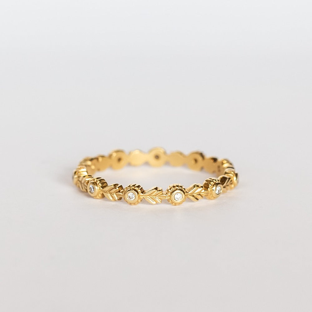 A yellow gold diamond eternity wedding band featuring leaf pattern accents alternating with bezel set diamonds with milgrain dot edges.