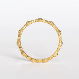 A yellow gold diamond eternity wedding band featuring leaf pattern accents alternating with bezel set diamonds with milgrain dot edges.