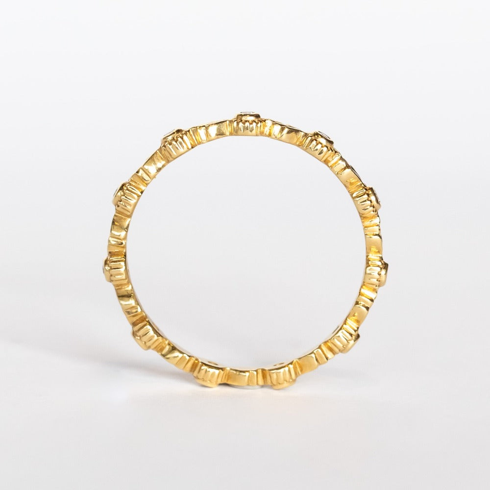 A yellow gold diamond eternity wedding band featuring leaf pattern accents alternating with bezel set diamonds with milgrain dot edges.