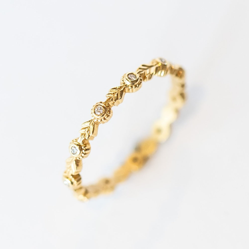 A yellow gold diamond eternity wedding band featuring leaf pattern accents alternating with bezel set diamonds with milgrain dot edges.