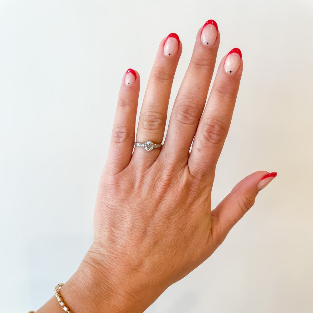 A platinum diamond engraved engagement ring with a bezel set old mine cut diamond center stone and a few diamond accents on each shoulder.