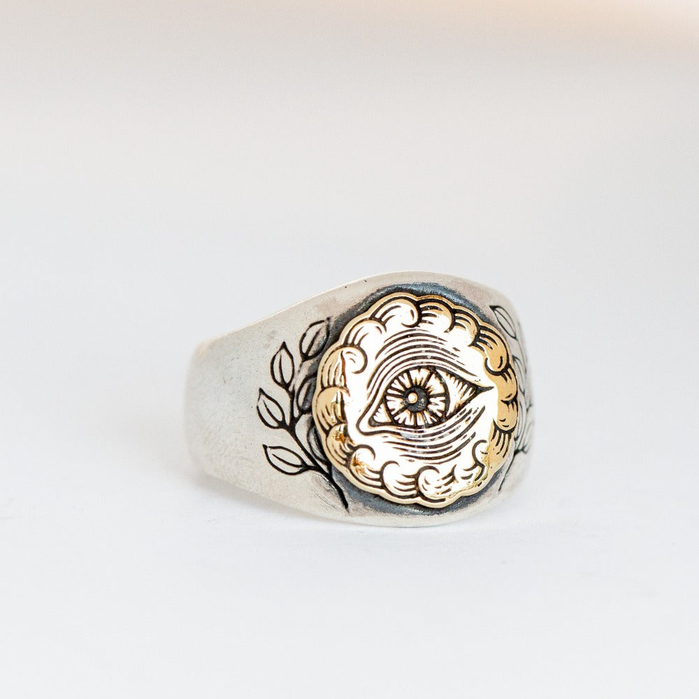 A chunky silver signet ring with yellow gold overlay, engraved with an all seeing eye symbol.