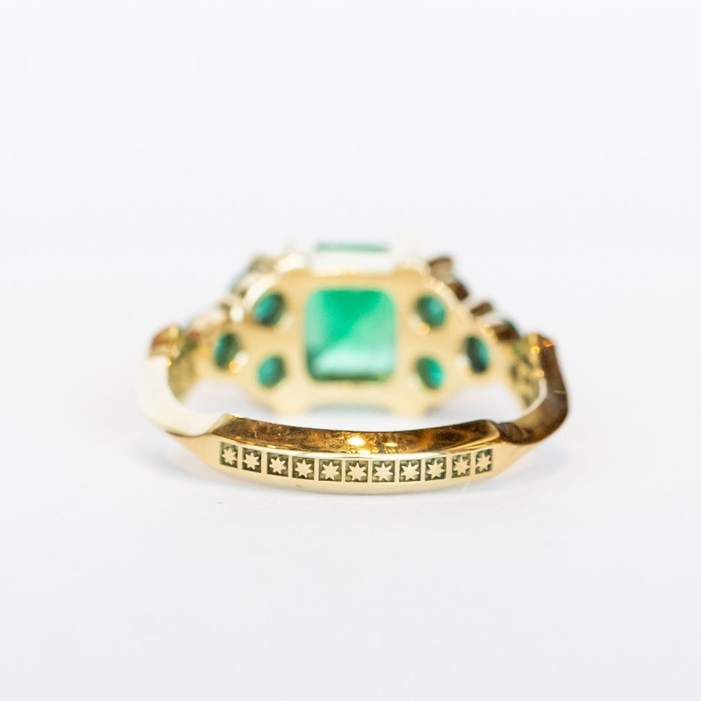 An emerald ring set of engagement ring and wedding band. Features an emerald cut emerald gemstone center flanked by six round emeralds, and a graduating size emerald band that contours to fit.