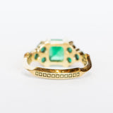 An emerald ring set of engagement ring and wedding band. Features an emerald cut emerald gemstone center flanked by six round emeralds, and a graduating size emerald band that contours to fit.