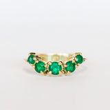 An emerald ring set of engagement ring and wedding band. Features an emerald cut emerald gemstone center flanked by six round emeralds, and a graduating size emerald band that contours to fit.