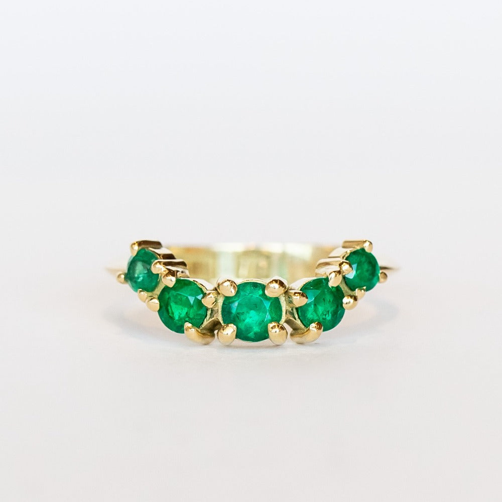 An emerald ring set of engagement ring and wedding band. Features an emerald cut emerald gemstone center flanked by six round emeralds, and a graduating size emerald band that contours to fit.