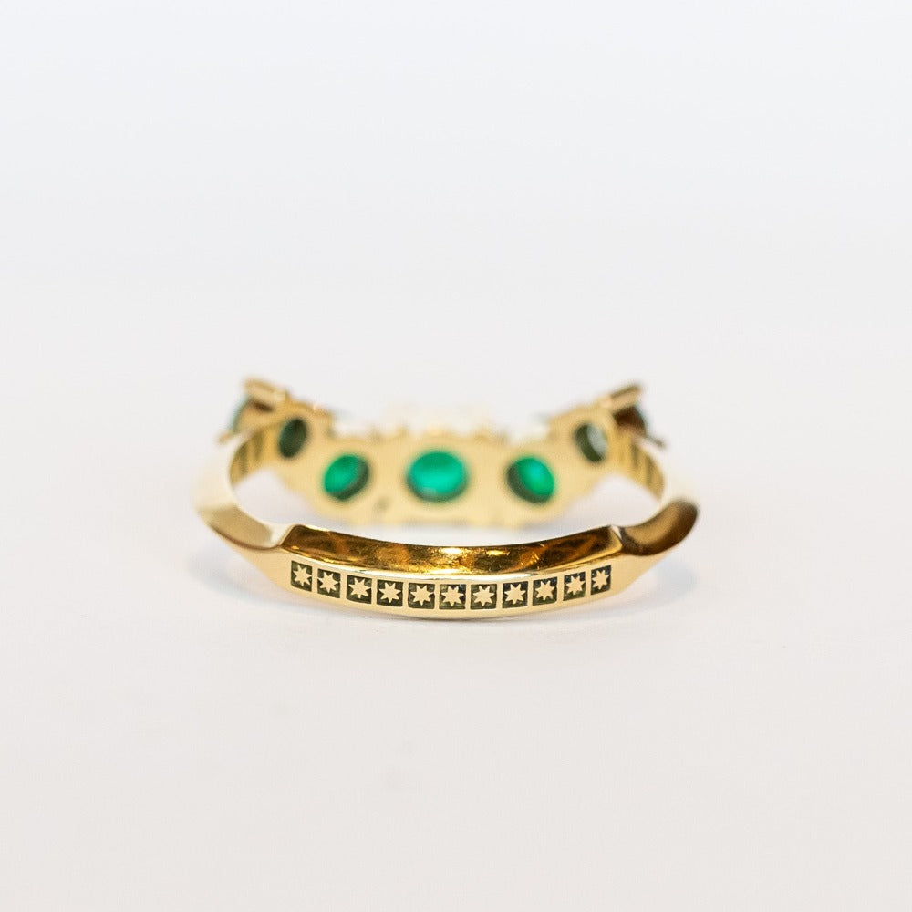 An emerald ring set of engagement ring and wedding band. Features an emerald cut emerald gemstone center flanked by six round emeralds, and a graduating size emerald band that contours to fit.