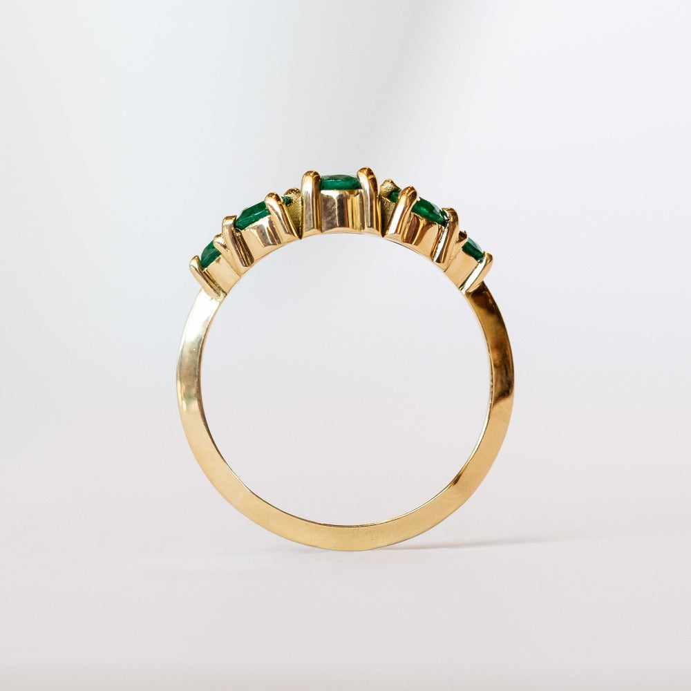 An emerald ring set of engagement ring and wedding band. Features an emerald cut emerald gemstone center flanked by six round emeralds, and a graduating size emerald band that contours to fit.