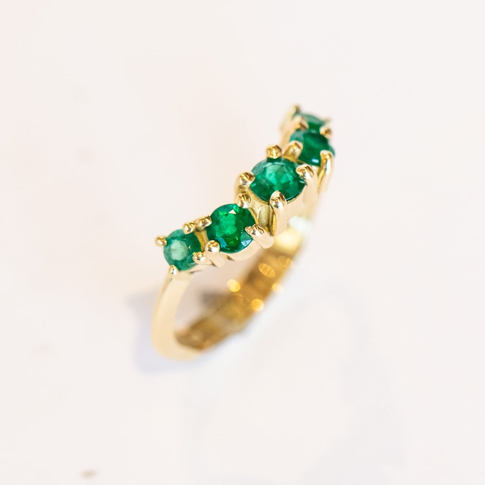 An emerald ring set of engagement ring and wedding band. Features an emerald cut emerald gemstone center flanked by six round emeralds, and a graduating size emerald band that contours to fit.