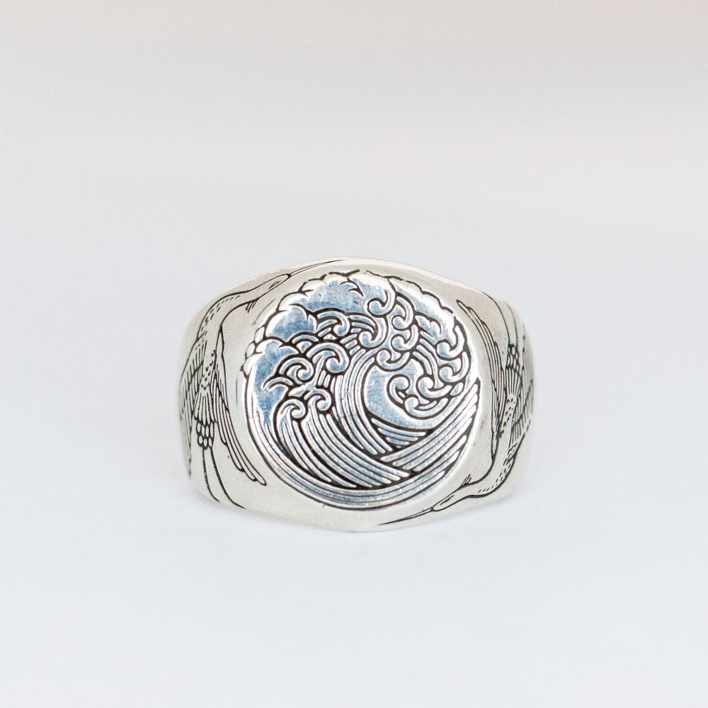 A chunky silver signet ring with a wave engraved into its face and a heron on each side.