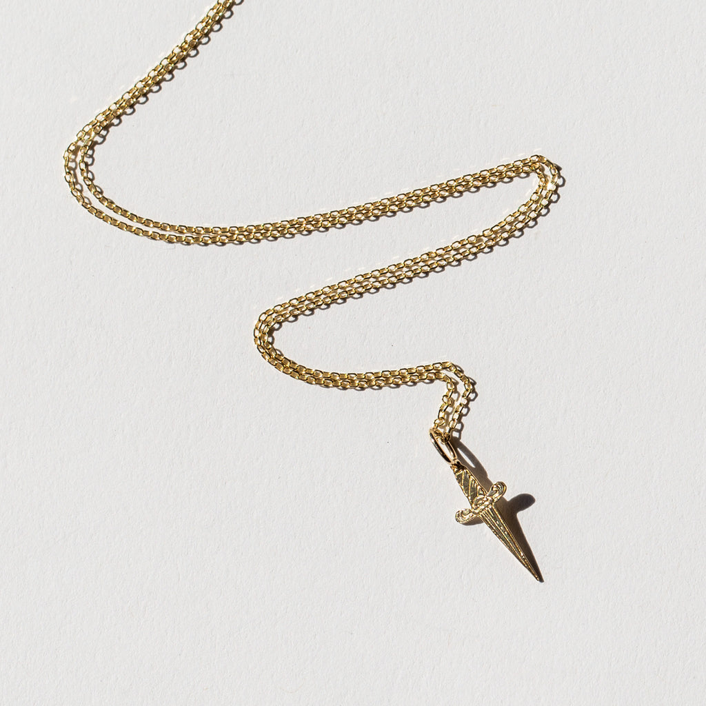 A tiny gold engraved dagger pendant necklace.