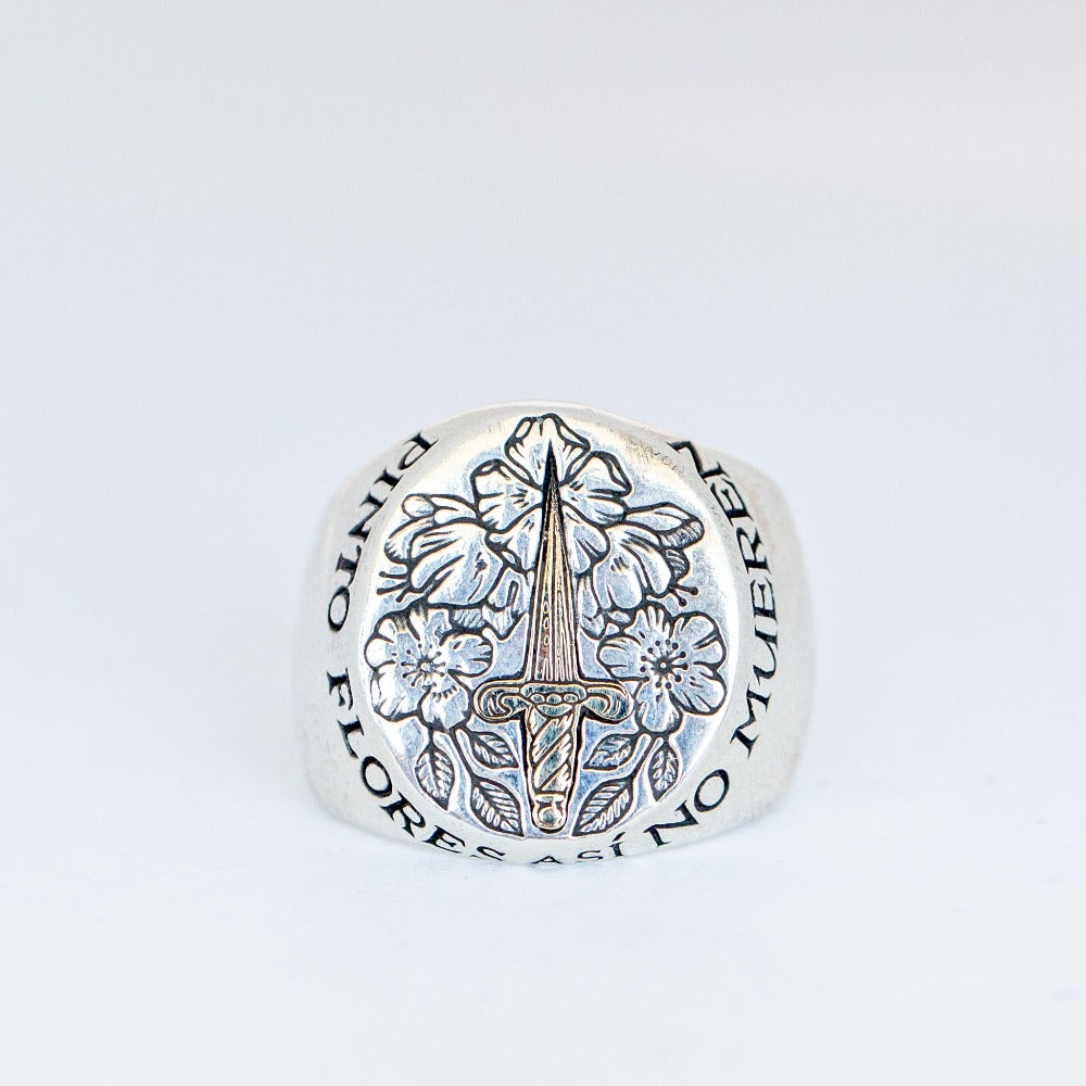 A chunky silver signet ring with gold dagger inlay featuring engraved flowers and a quote from Frida Khalo.