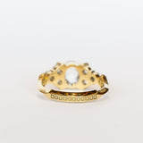 A diamond engagement ring featuring salt and pepper diamonds, an oval at the center, flanked by clusters of three smaller diamonds on each side, set in 18 karat yellow gold.