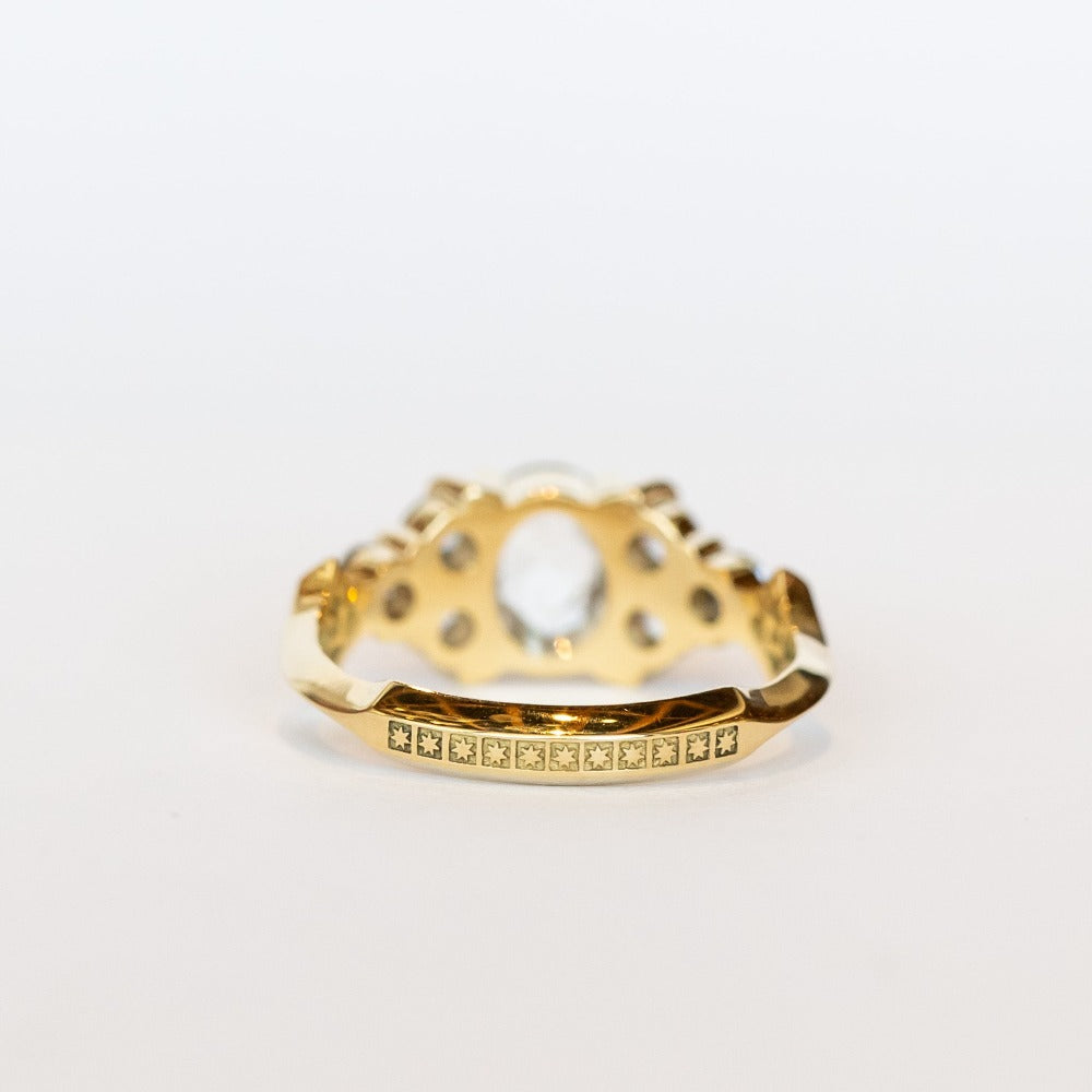 A diamond engagement ring featuring salt and pepper diamonds, an oval at the center, flanked by clusters of three smaller diamonds on each side, set in 18 karat yellow gold.