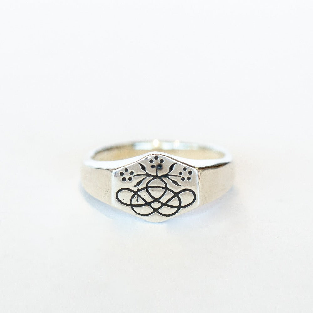 A dainty silver signet ring engraved with a small bouquet and ribbon posey design.