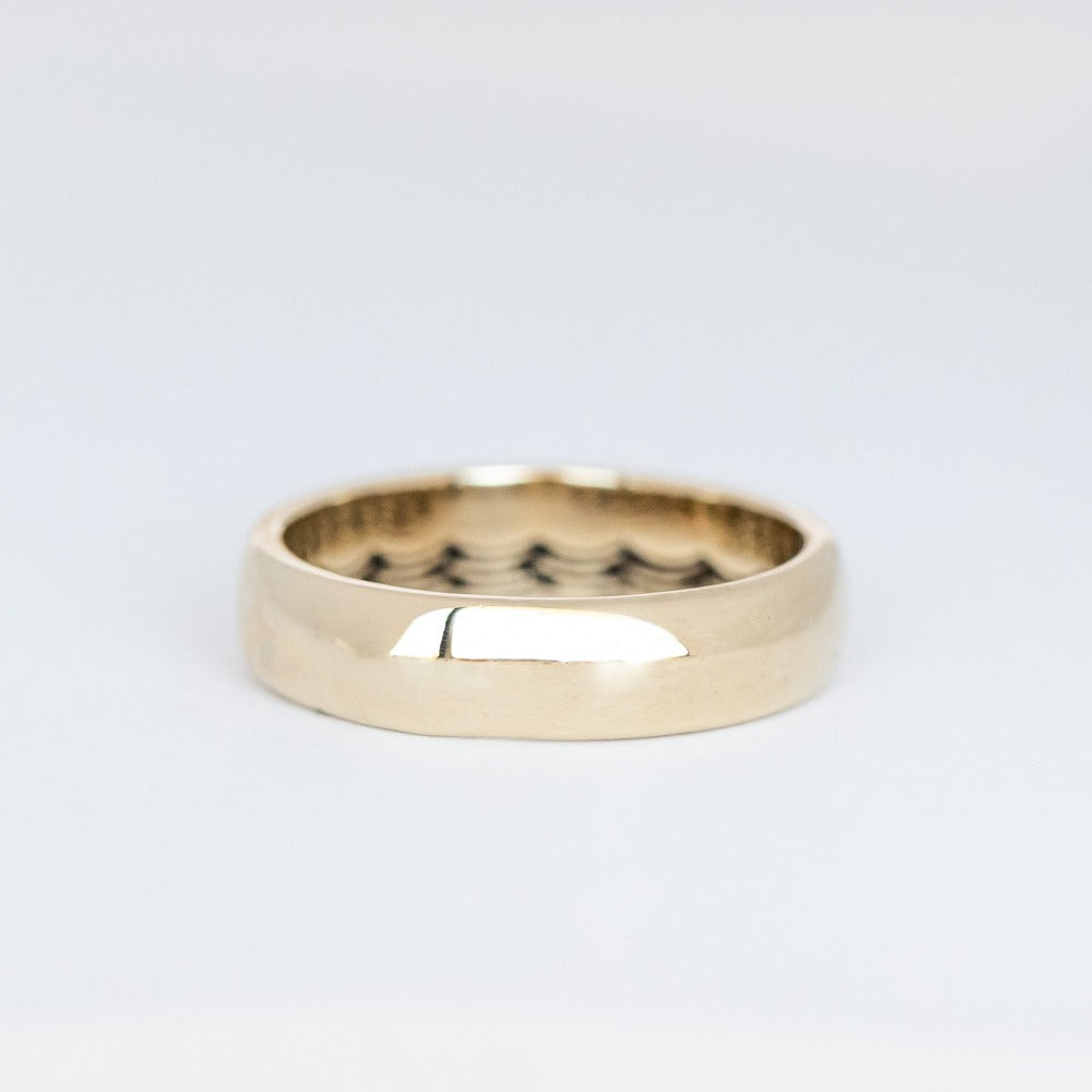 Domed gold wedding band featuring a wave pattern engraving that wraps all the way around the inside.