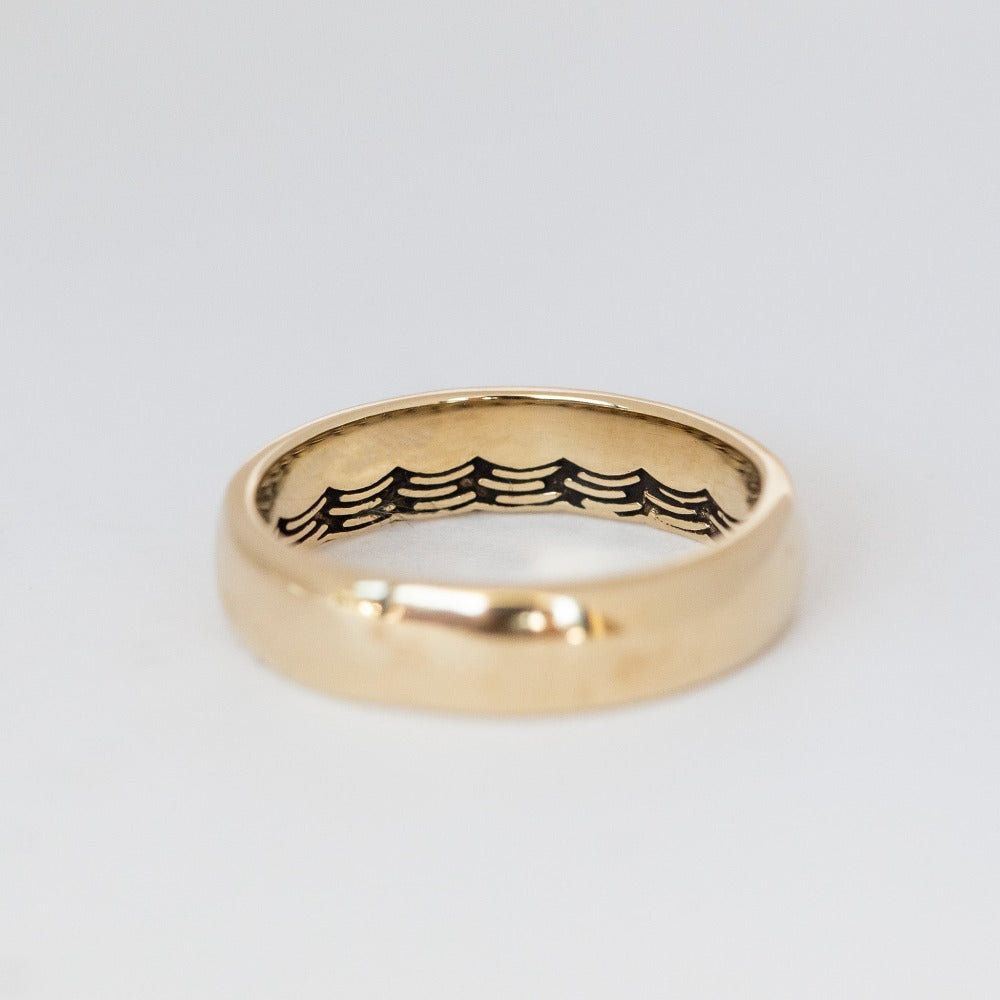 Domed gold wedding band featuring a wave pattern engraving that wraps all the way around the inside.