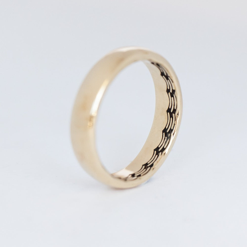 Domed gold wedding band featuring a wave pattern engraving that wraps all the way around the inside.