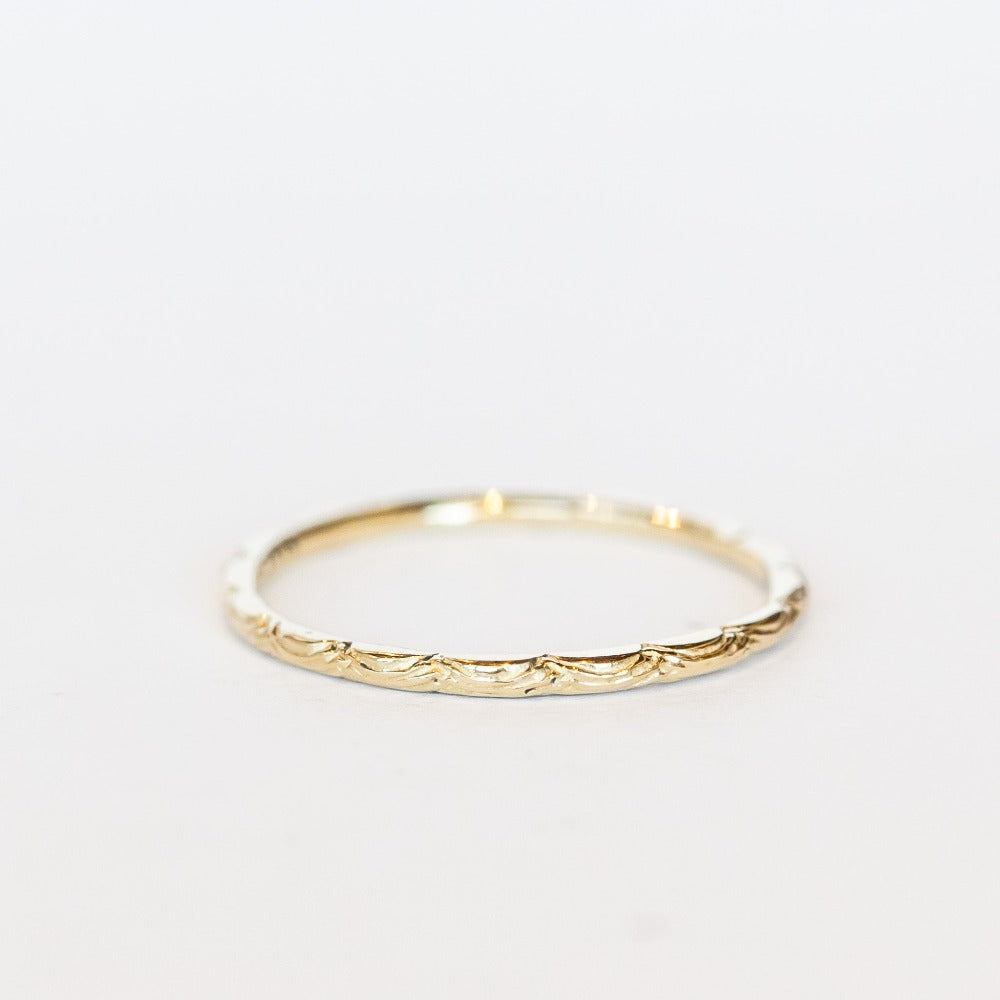 A dainty gold band with an intricate wave pattern all the way around.