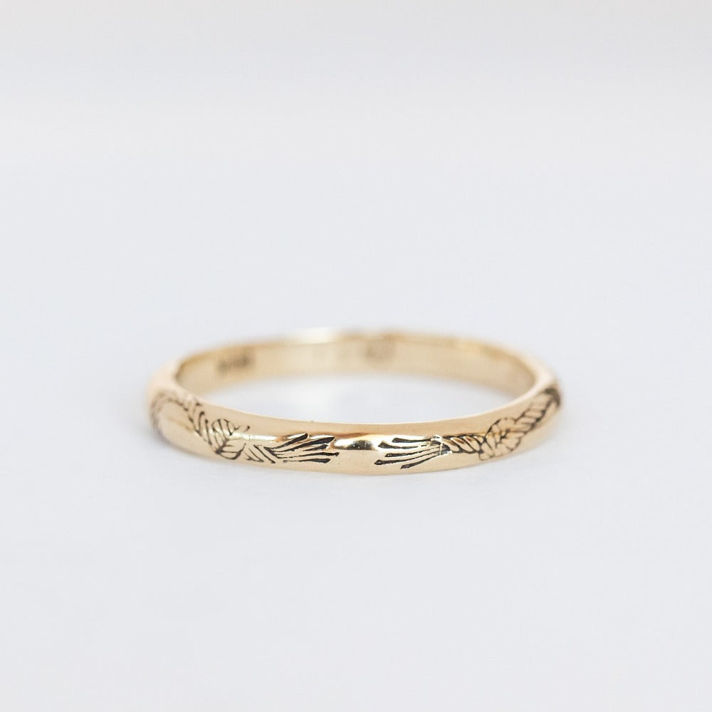 An engraved gold band with a domed contour and knotted rope engraving that encircles the band.