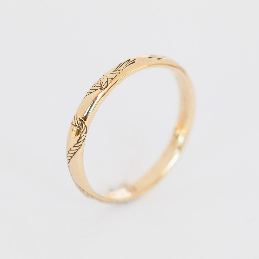 An engraved gold band with a domed contour and knotted rope engraving that encircles the band.