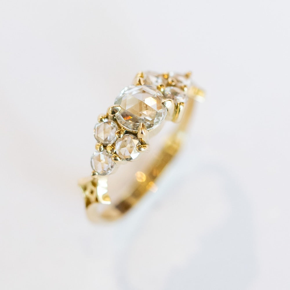 A diamond engagement ring that features a 1 carat rose cut center stone flanked by six rose cut side stones, in a polished 18k yellow gold setting.