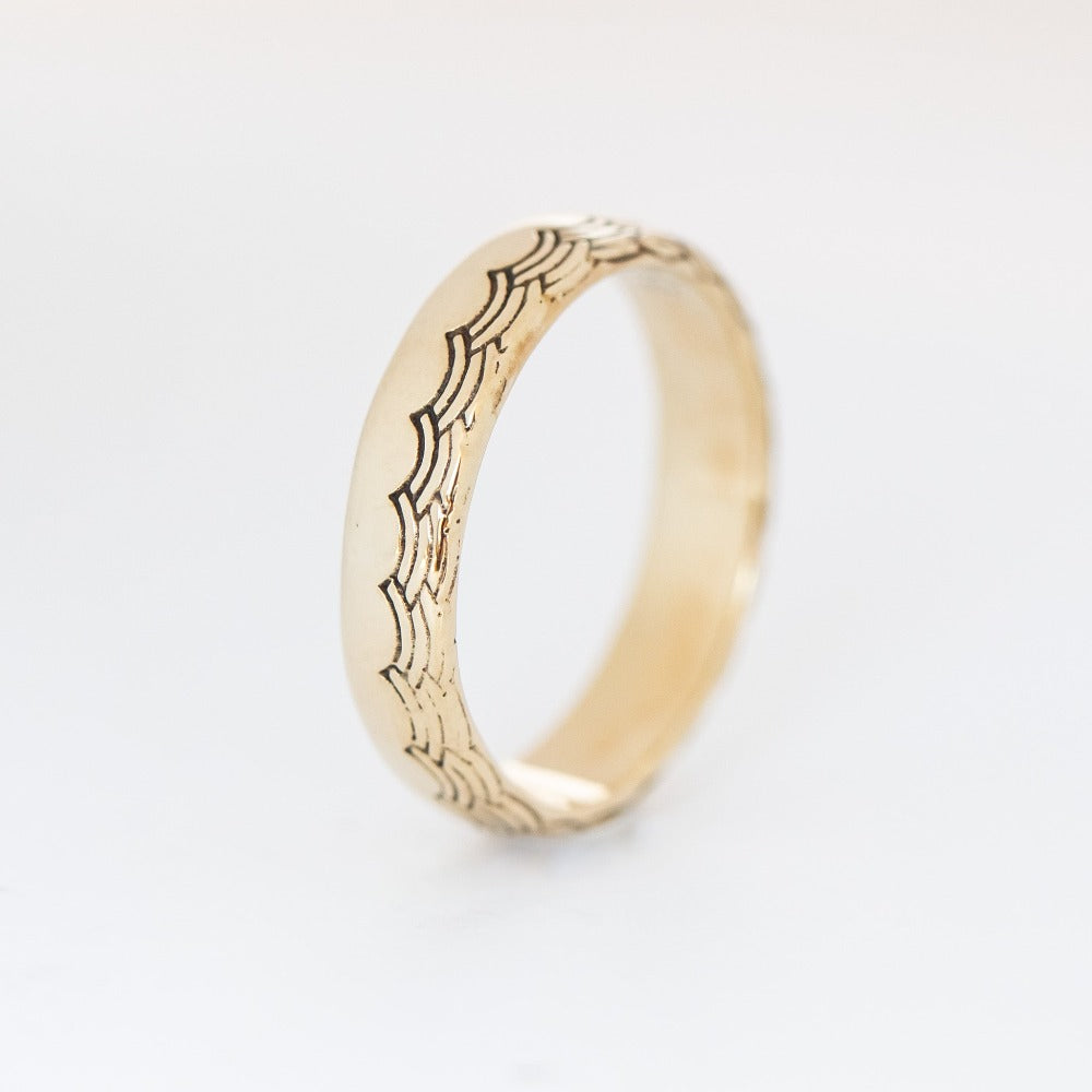 A 5mm half-dome gold band with a wave pattern engraving along one edge that wraps around the entire band.