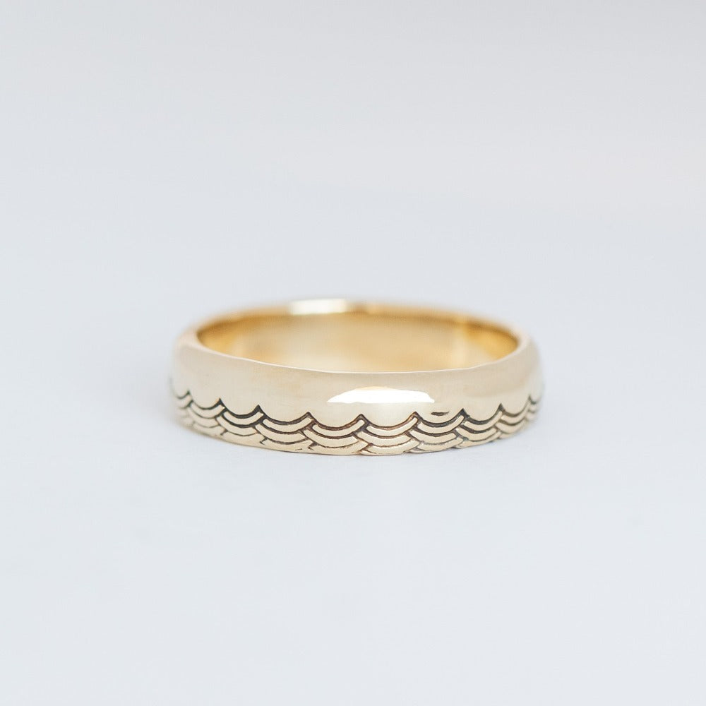 A 5mm half-dome gold band with a wave pattern engraving along one edge that wraps around the entire band.