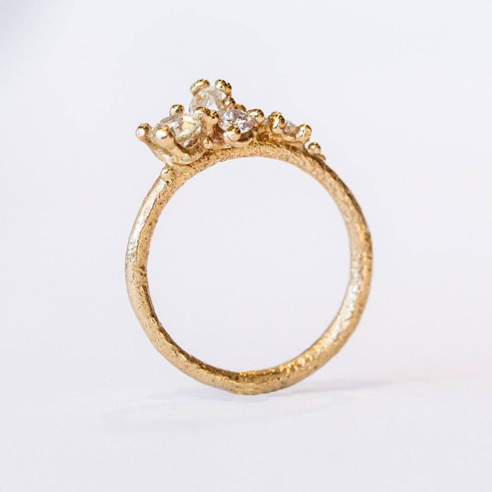 A tapering cluster of antique cut white diamonds all nestled amongst polished granules of rich yellow gold on a textured band.