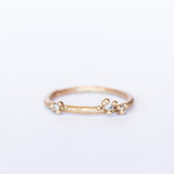 A delicate wedding band or stacking ring featuring white diamonds in two asymmetrical clusters set amongst granules of yellow gold.