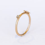 A delicate wedding band or stacking ring featuring white diamonds in two asymmetrical clusters set amongst granules of yellow gold.