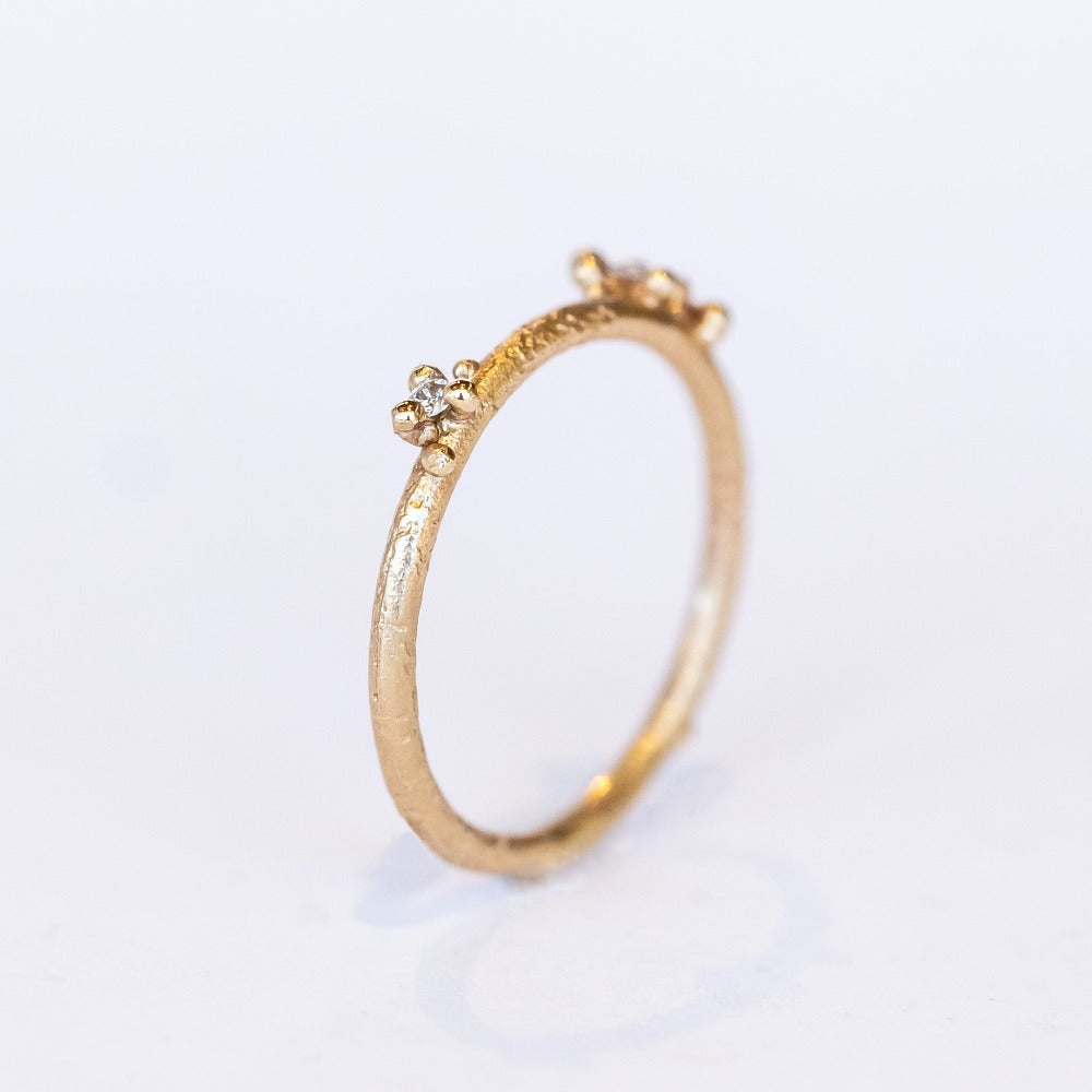 A delicate wedding band or stacking ring featuring white diamonds in two asymmetrical clusters set amongst granules of yellow gold.