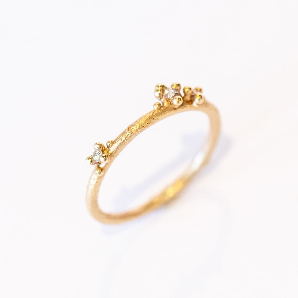 A delicate wedding band or stacking ring featuring white diamonds in two asymmetrical clusters set amongst granules of yellow gold.