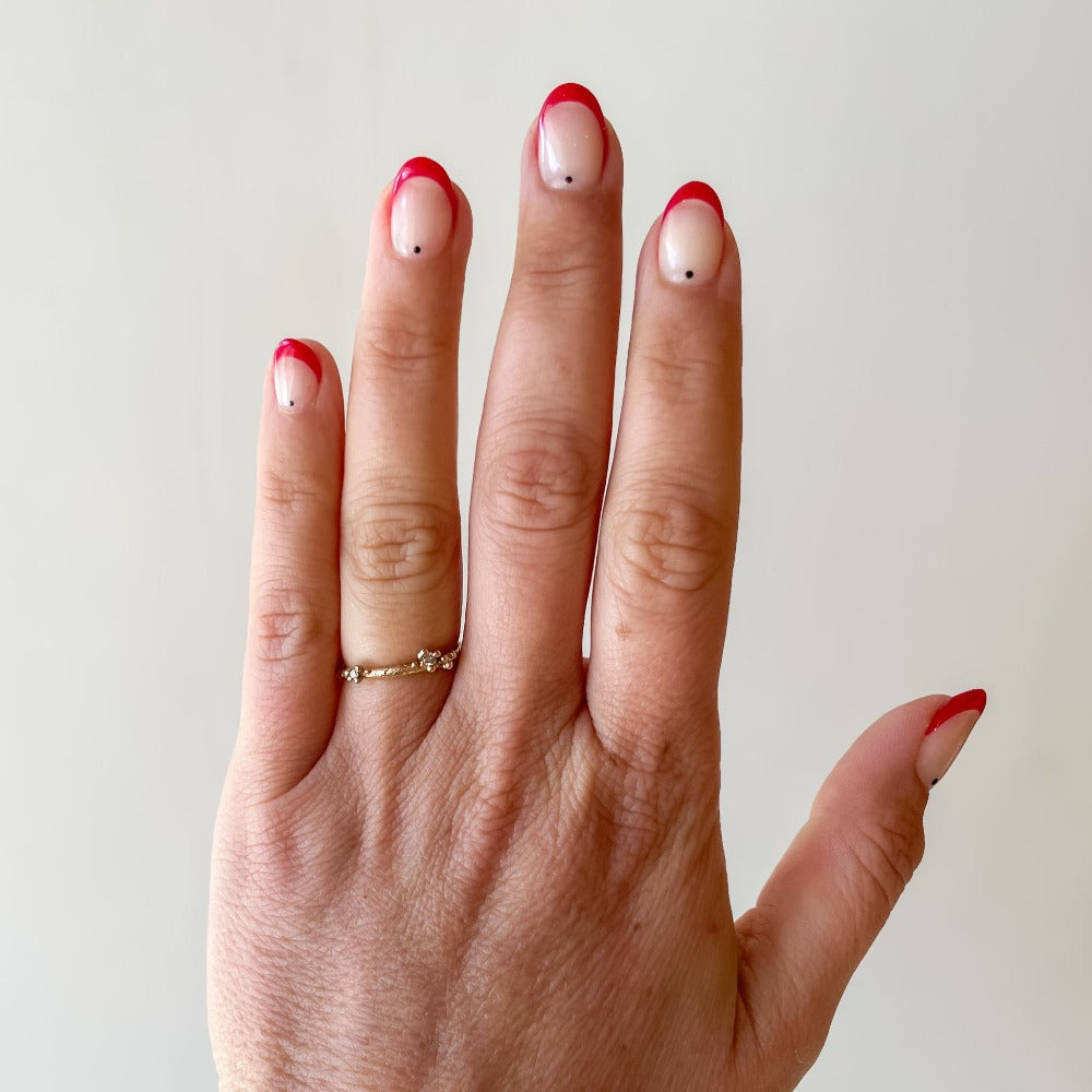 A delicate wedding band or stacking ring featuring white diamonds in two asymmetrical clusters set amongst granules of yellow gold. On hand.