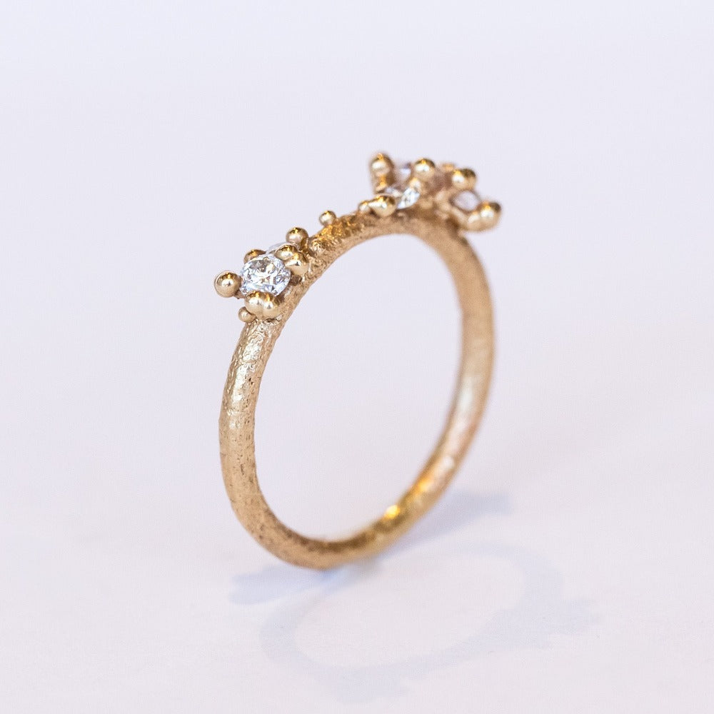 A textured gold band set with asymmetric clusters of small diamonds.
