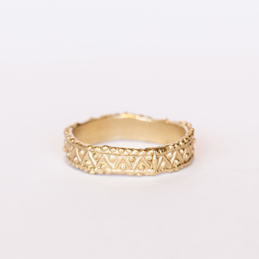 A wide gold wedding band with intricate zig zag and dot detailing.
