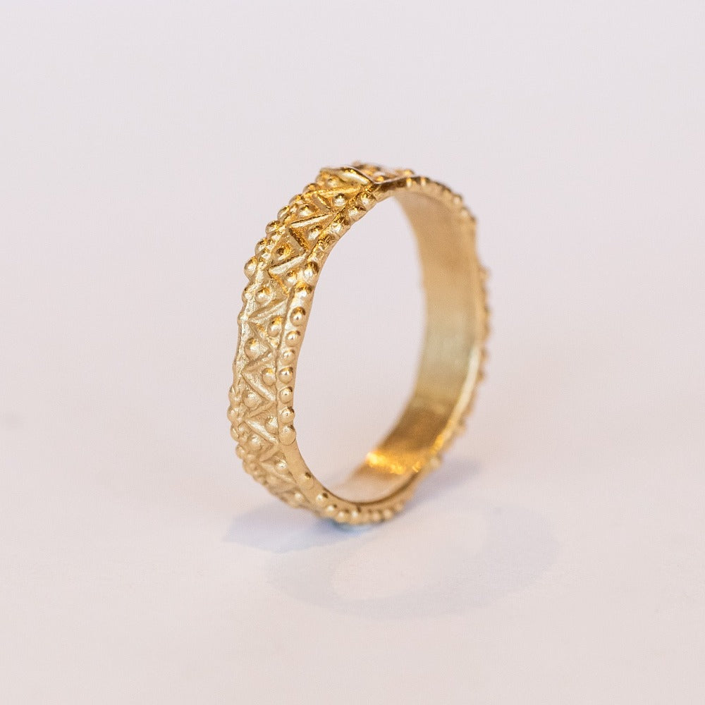 A wide gold wedding band with intricate zig zag and dot detailing.