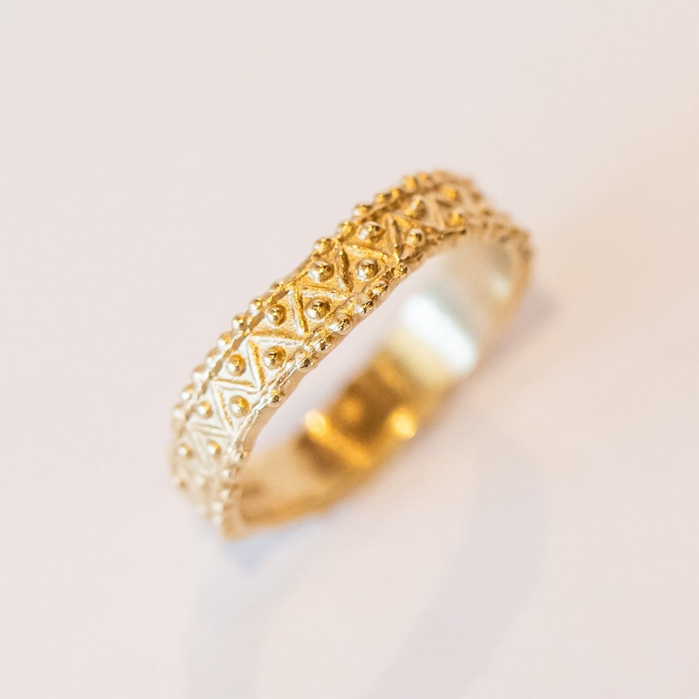 A wide gold wedding band with intricate zig zag and dot detailing.