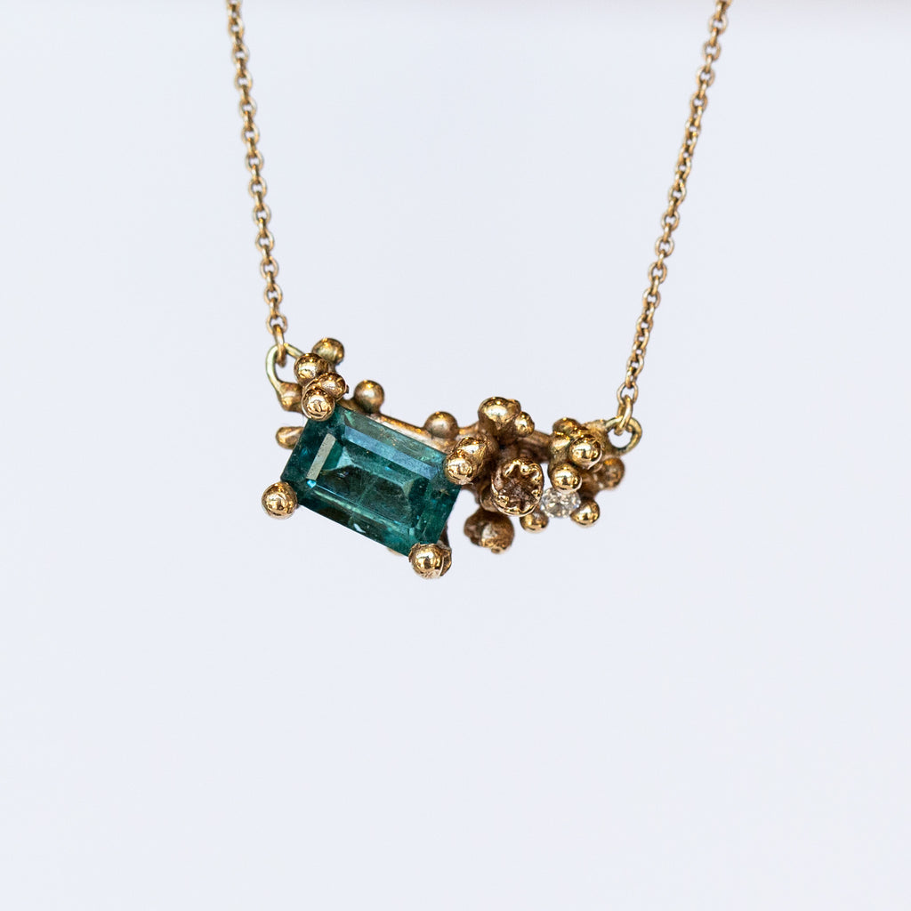 A yellow gold pendant necklace featuring a rectangular green tourmaline and tiny accent diamond set into a cluster of golden granules.