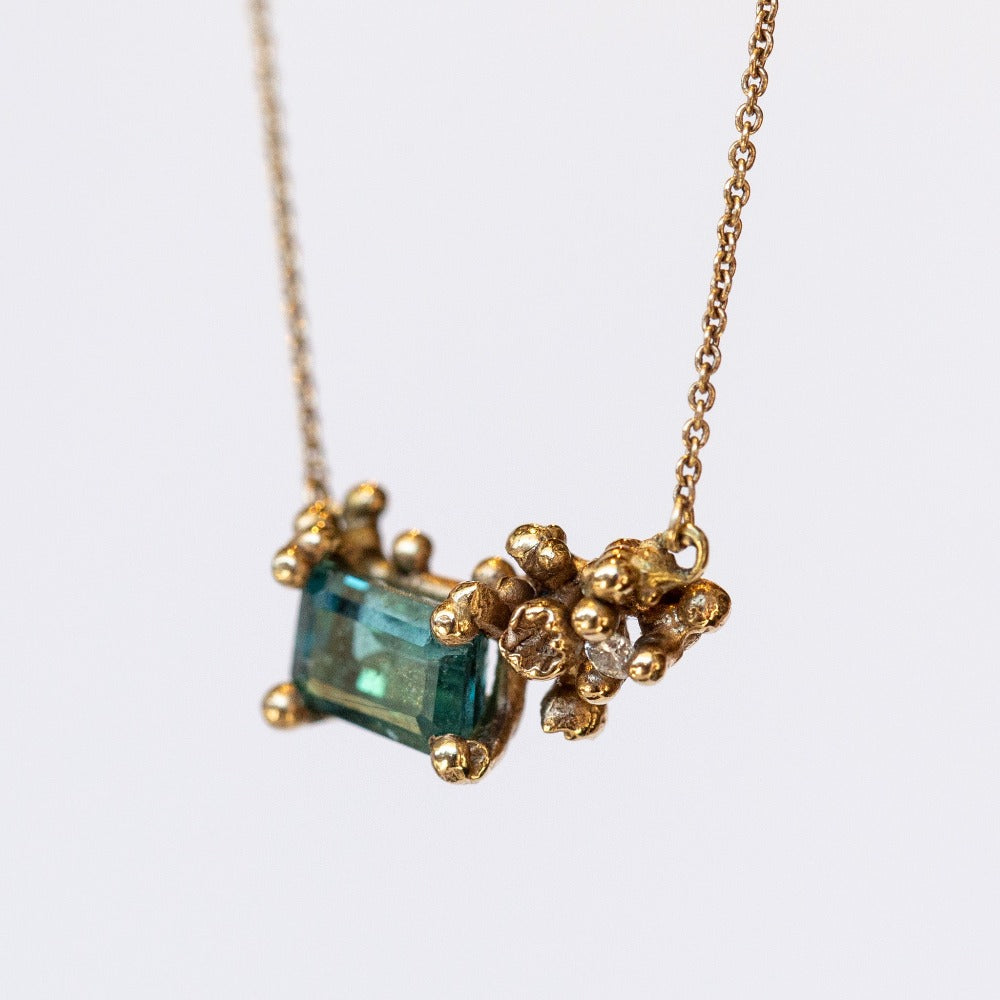 A yellow gold pendant necklace featuring a rectangular green tourmaline and tiny accent diamond set into a cluster of golden granules.