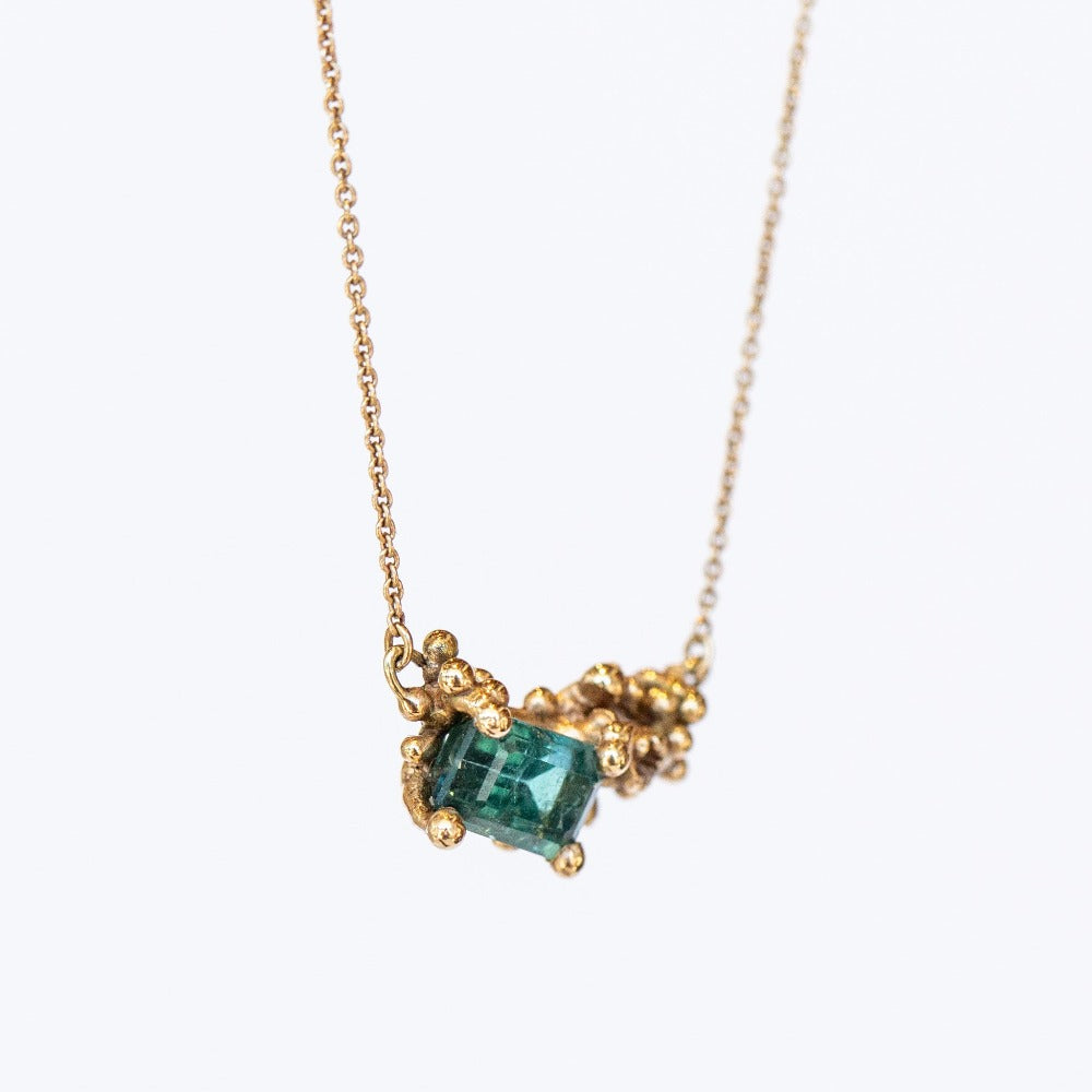 A yellow gold pendant necklace featuring a rectangular green tourmaline and tiny accent diamond set into a cluster of golden granules.