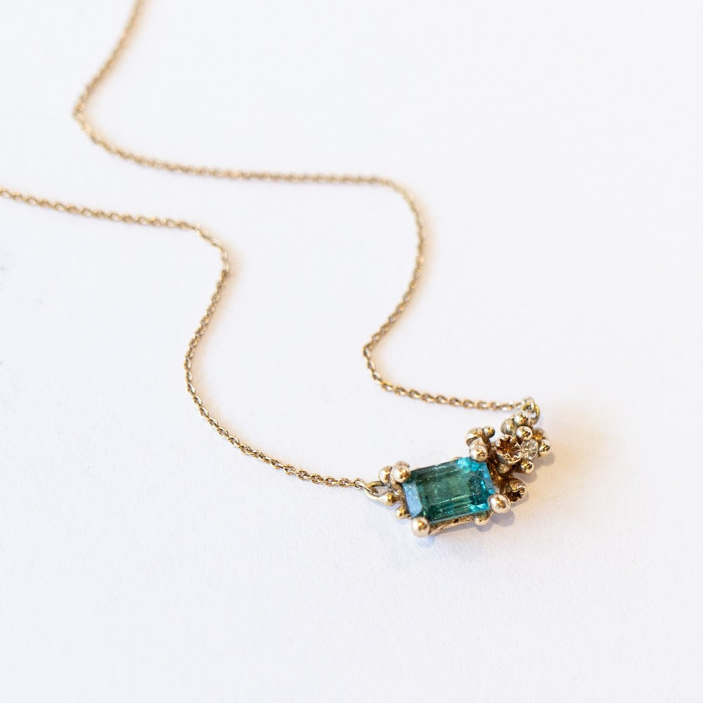 A yellow gold pendant necklace featuring a rectangular green tourmaline and tiny accent diamond set into a cluster of golden granules.