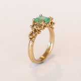 A yellow gold ring featuring an Asscher cut pale green emerald and clusters of diamonds to either side set in granulation.