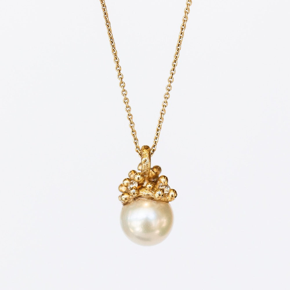 A cluster of golden granules holds a white pearl in this pendant necklace on a cable chain.