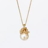 A cluster of golden granules holds a white pearl in this pendant necklace on a cable chain.