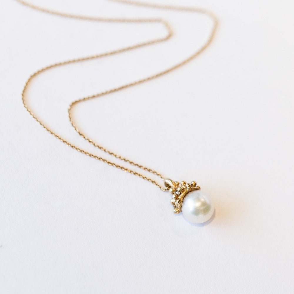 A cluster of golden granules holds a white pearl in this pendant necklace on a cable chain.