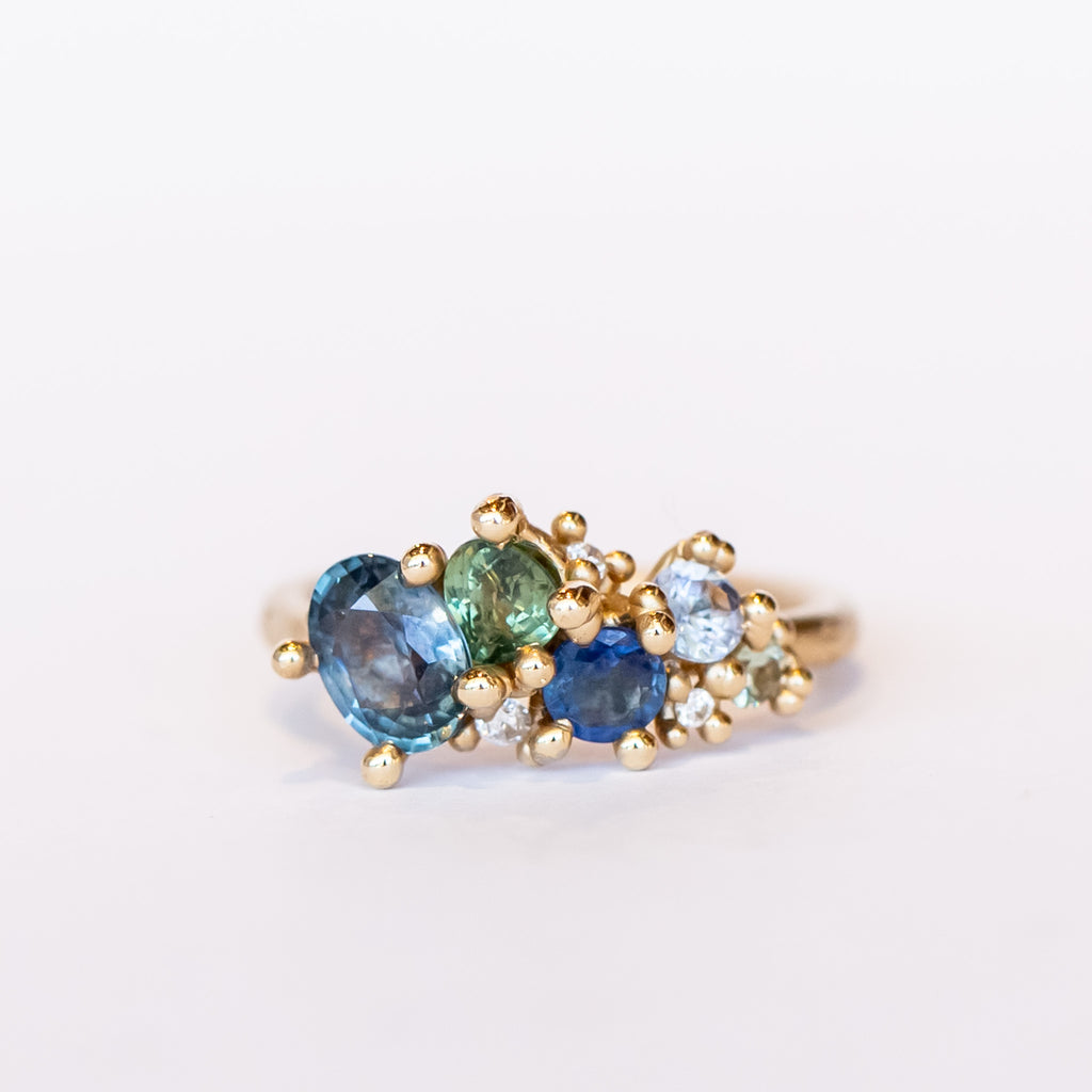 An asymmetrical cluster ring set with green and blue sapphires amongst gold granules with a lightly textured band.