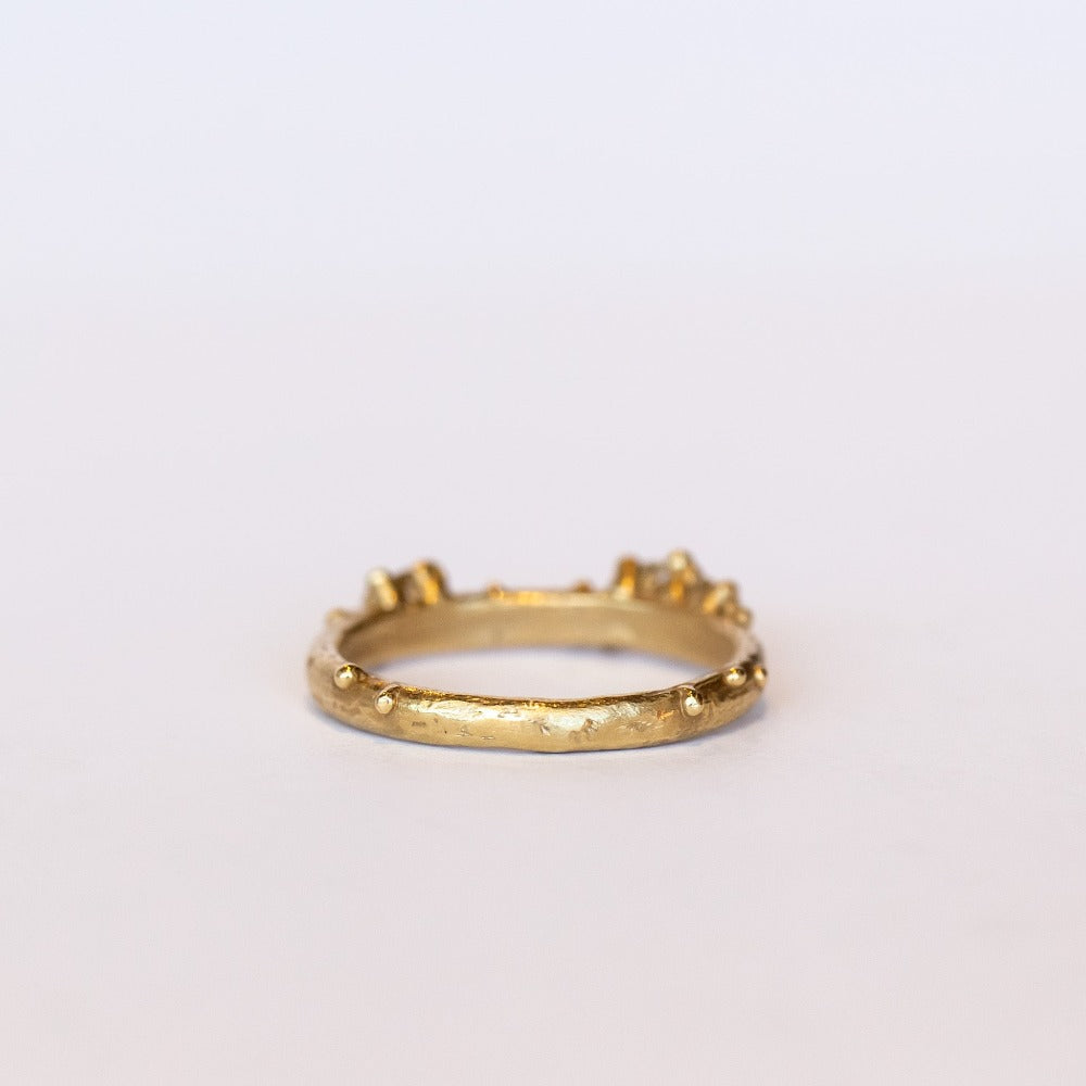 A stackable band featuring five white diamonds nestling amongst granules of yellow gold on a gently textured half round band.