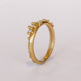 A stackable band featuring five white diamonds nestling amongst granules of yellow gold on a gently textured half round band.